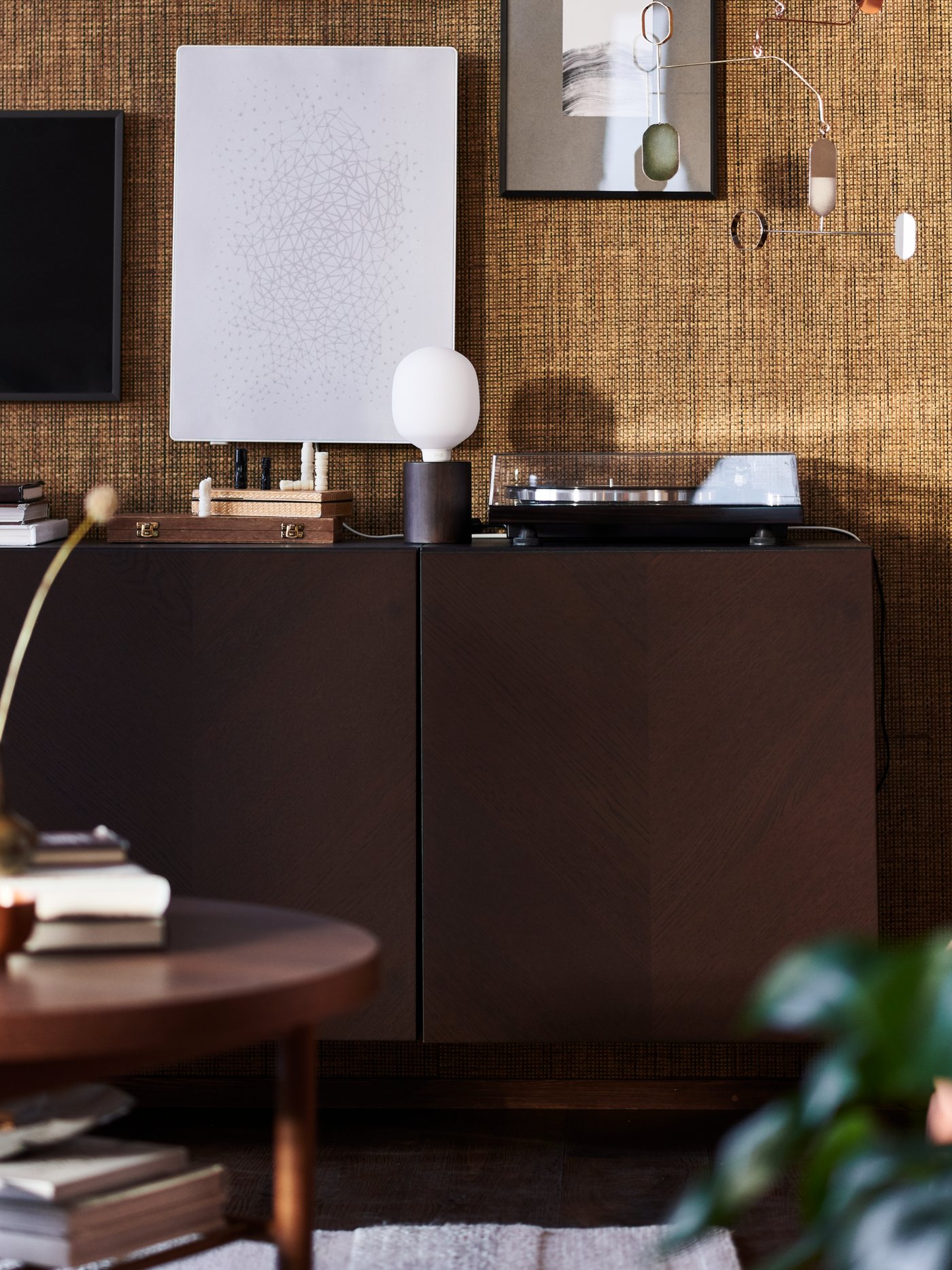 A dark-brown BESTÅ cabinet in a brown room, with a BLEKKLINT table lamp and a SYMFONISK picture frame with WiFi speaker.