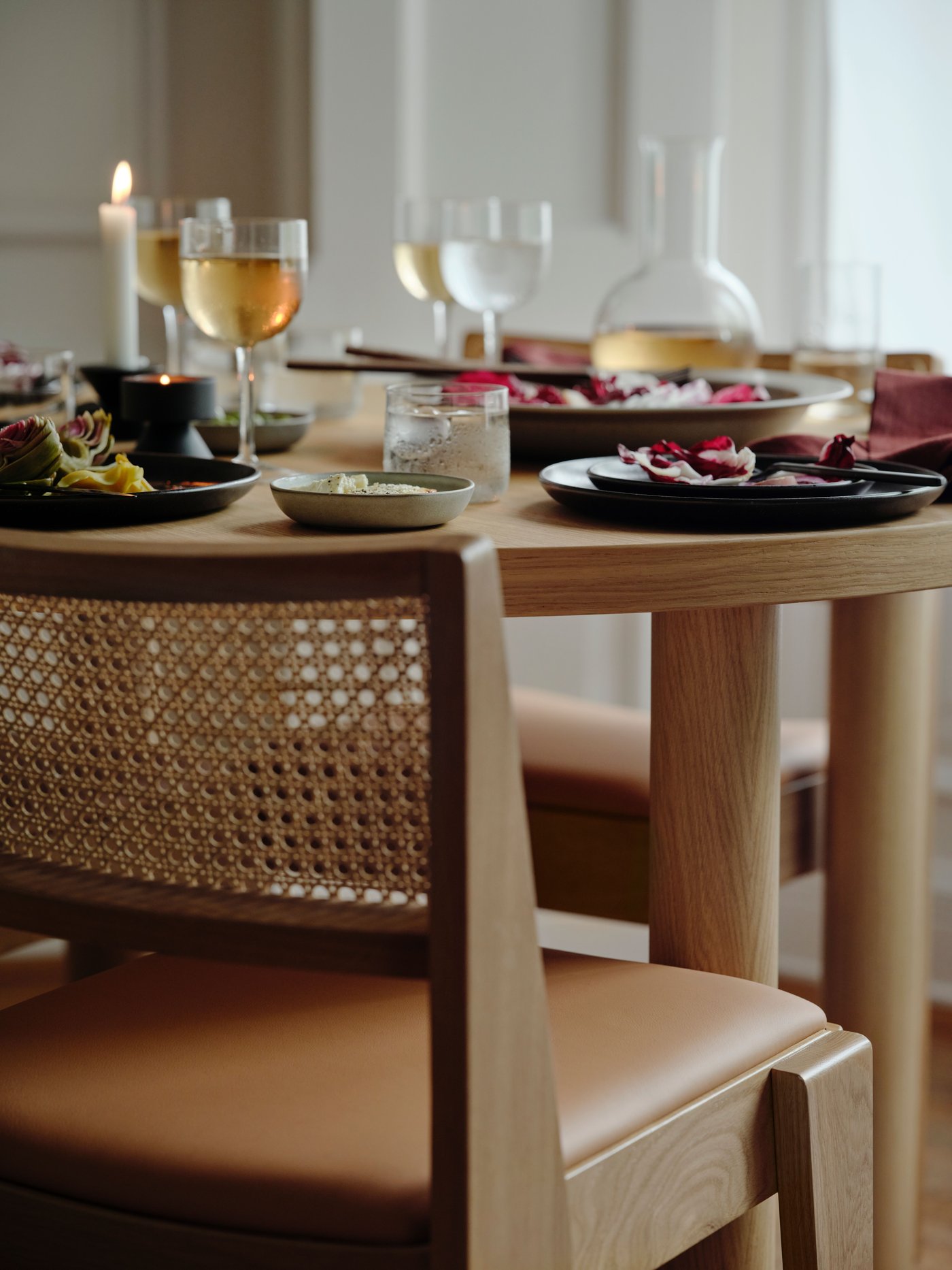 A STOCKHOLM 2025 oak veneer table set with plates and side plates, wine glasses, a carafe, and a lit candle.
