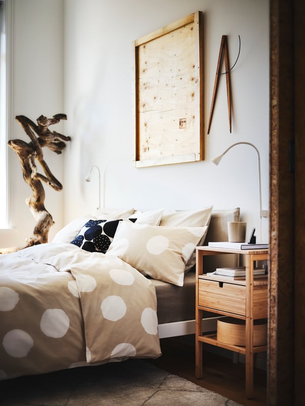 A KLEPPSTAD bed with a KLYNNETÅG duvet cover sits next to a wooden NORDKISA bedside table and a NÄVLINGE LED spotlight.