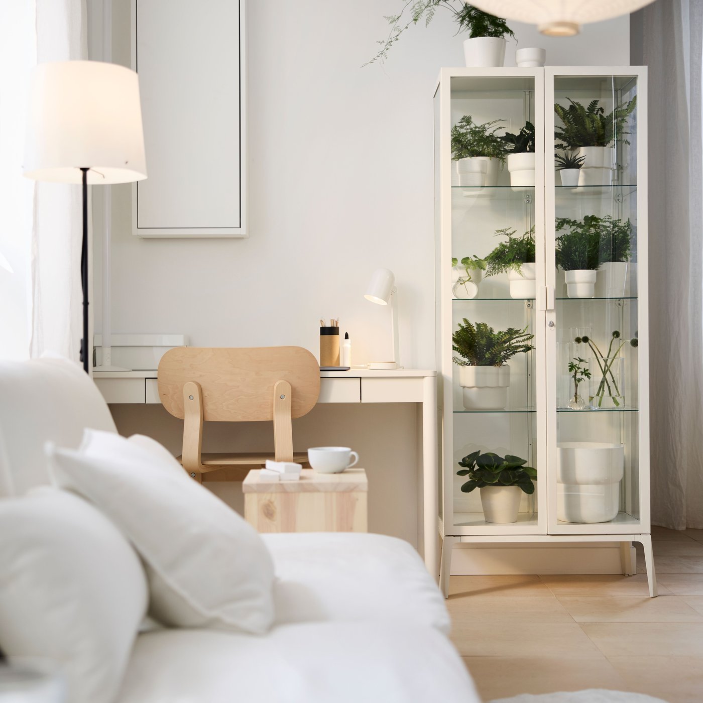 Dans une pièce multifonctionnelle, espace de travail meublé d’un bureau TONSTAD blanc et d’une chaise, et vitrine MILSBO garnie de plantes.