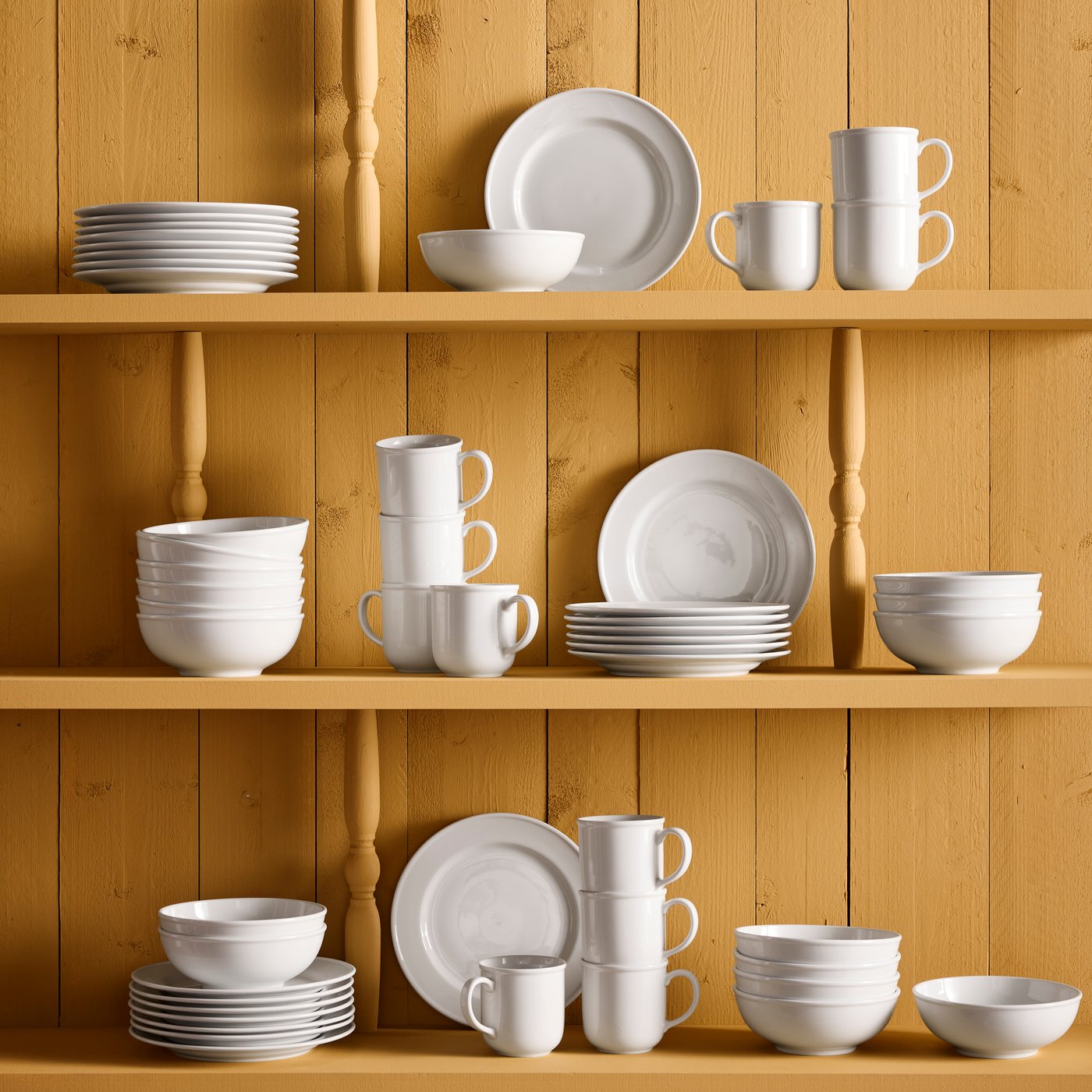Stacks of VARDAGEN bowls, plates and mugs are on yellow shelves against a yellow wall.
