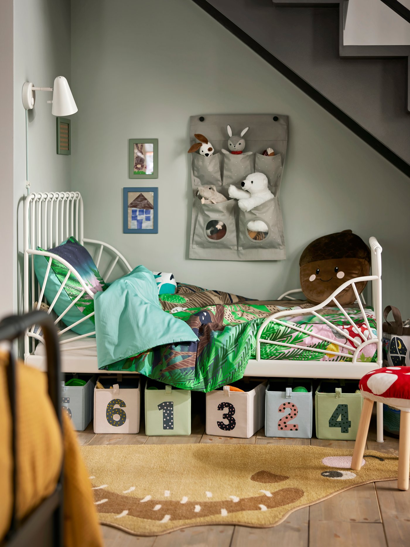 Una habitación infantil con una cama extensible IKEA. Debajo de la cama hay cajas con numeros y en la pared del costado de la cama se ven peluches en un organizador.
