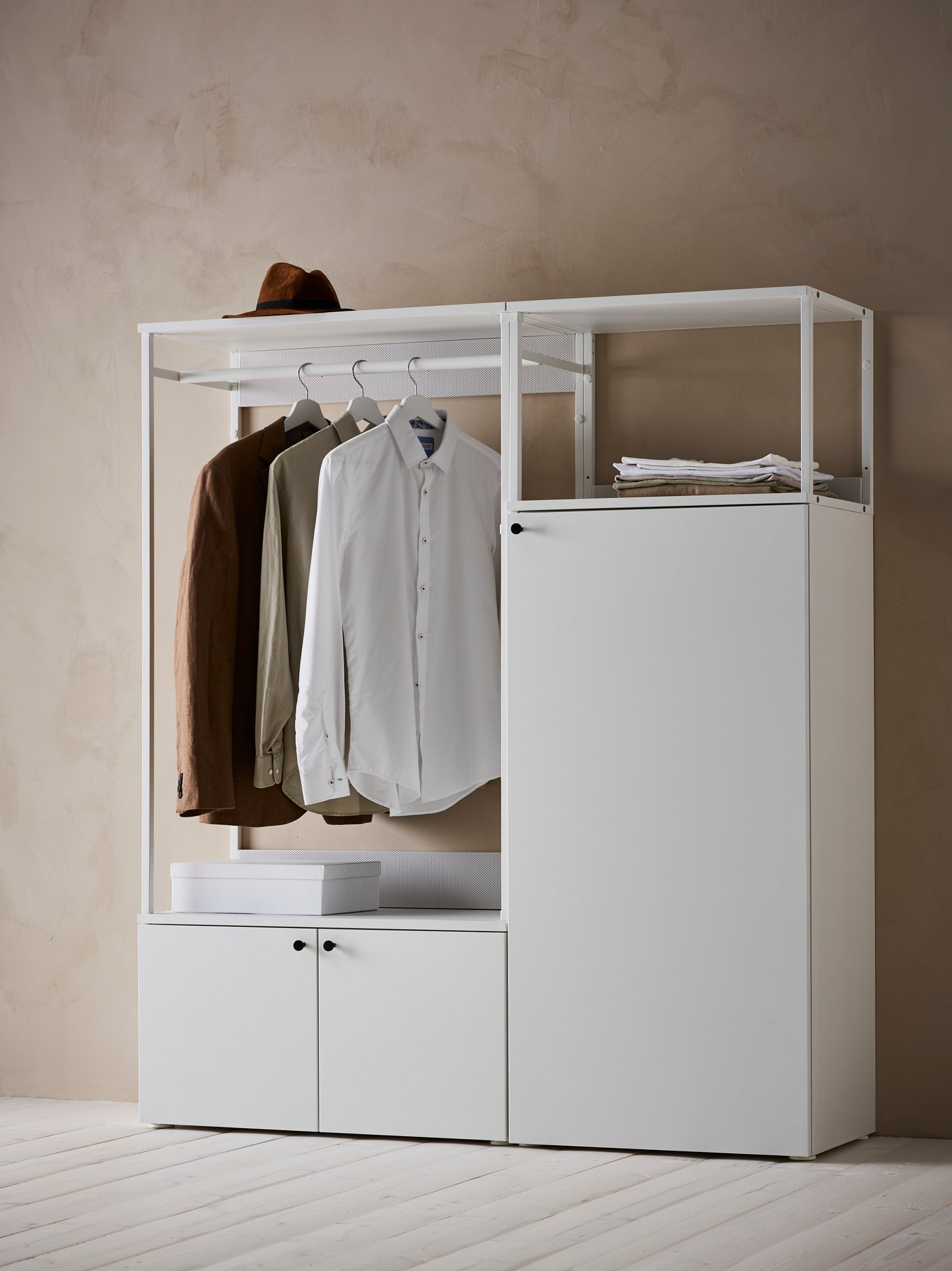 A white PLATSA wardrobe with three doors has a box and papers on its shelves, a hat on top and shirts hanging from the rail.