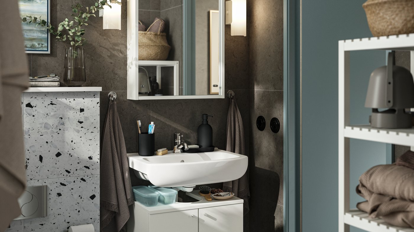 A small bathroom with dark brown walls and white furniture. A NYSJÖN cabinet with two doors holds storage under the sink.