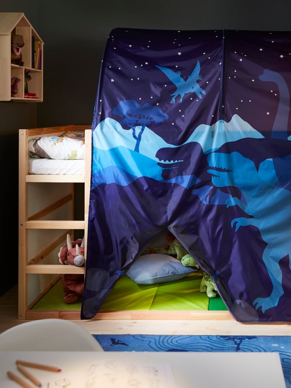 A KURA reversible bed set high with a KURA bed tent and JÄTTELIK bed linen, with a PLUFSIG folding gym mat underneath.