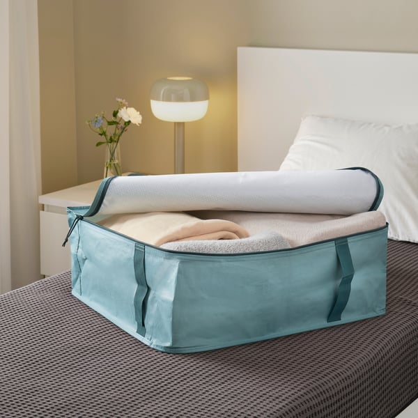 Eine türkise SÄCKKÄRRA Aufbewahrungsbox auf einem Bett.