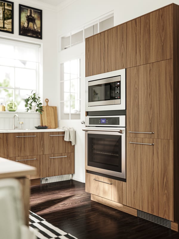 Une cuisine avec une armoire et des tiroirs dotés de façades TISTORP à effet noyer brun, et quelques électroménagers encastrables.