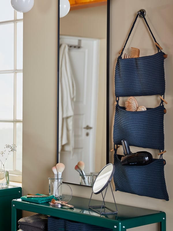 A bathroom beauty station that consists of NORDRANA hanging storage, a wall-mounted mirror and a green shelving unit.