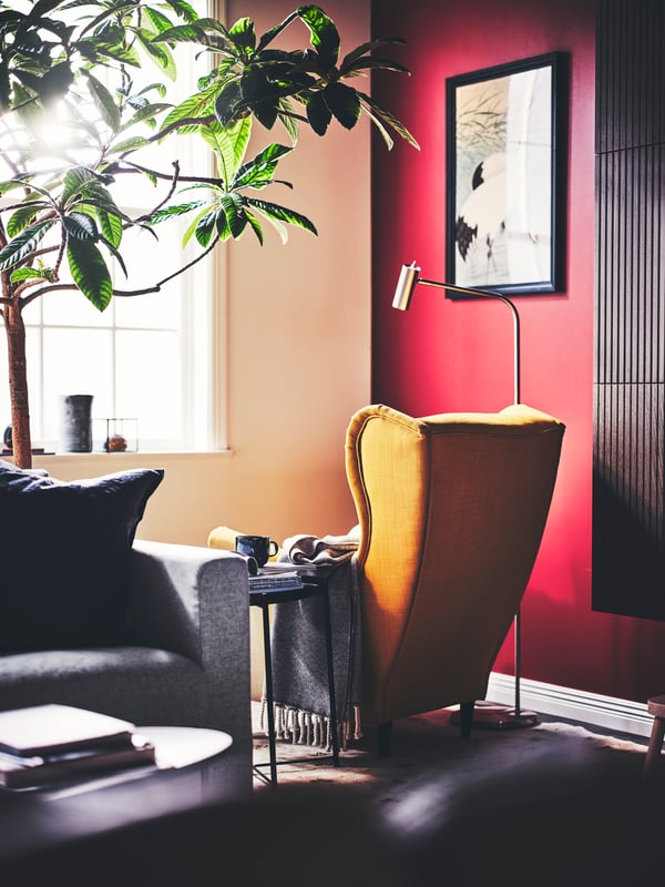 A living room with a yellow STRANDMON wing chair with ULLTISTEL throw, a black GLADOM tray table, and a VIRRMO floor lamp.
