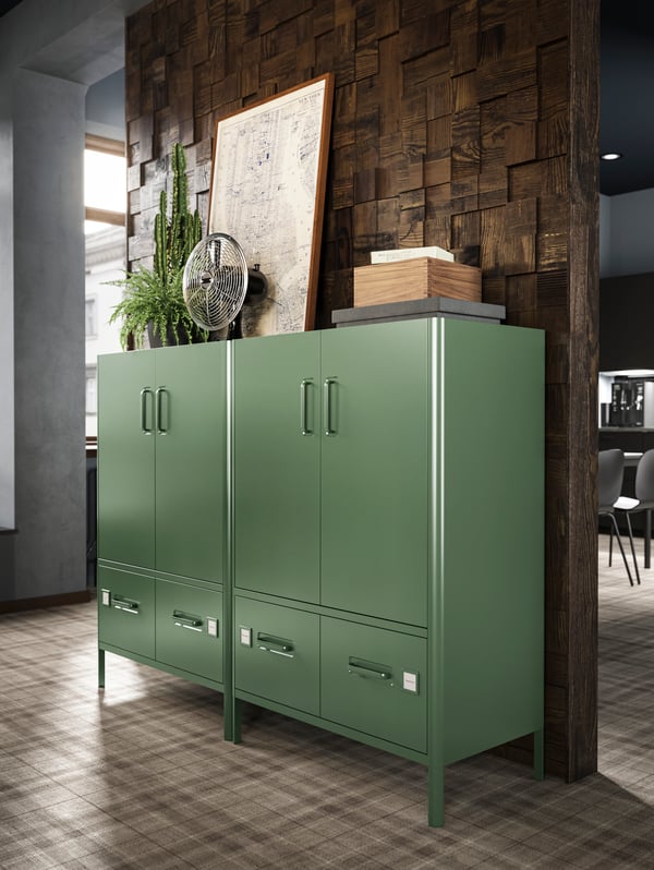 Two side-by-side, dark-green IDÅSEN cabinets with doors and drawers by a wall of dark wood set in mosaic-style relief.