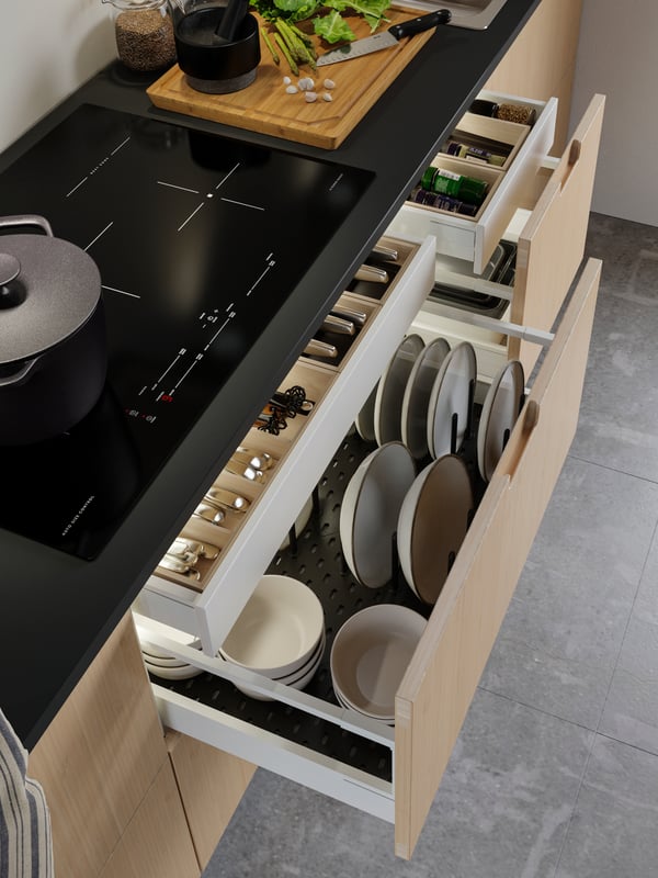 An open kitchen drawer with bamboo cutlery trays, and plates on an anthracite pegboard drawer organizer.