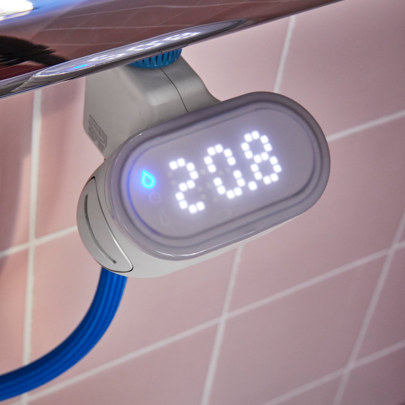 Compteur d’eau pour douche BERGVATTNET connecté à un mitigeur thermostatique pour douche et un flexible bleu dans une douche carrelée.