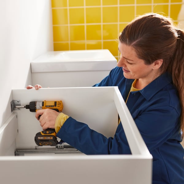 An IKEA bathroom installer installing a cabinet with a drill.