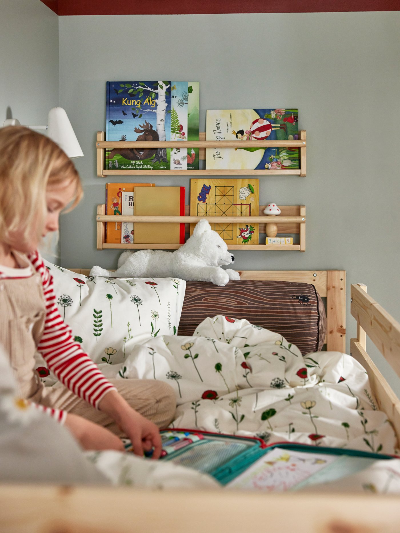 Close-up of little girl sitting in the top bed of MYDAL bunk bed, with FLISAT shelfs in the back, loaded with books.
