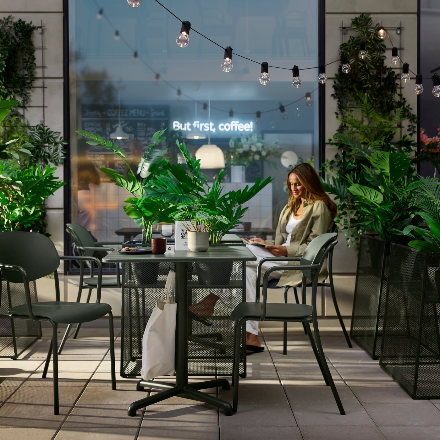 Café serving area outdoors featuring deep green VISINGSÖ tables, metal chairs and a person reading.