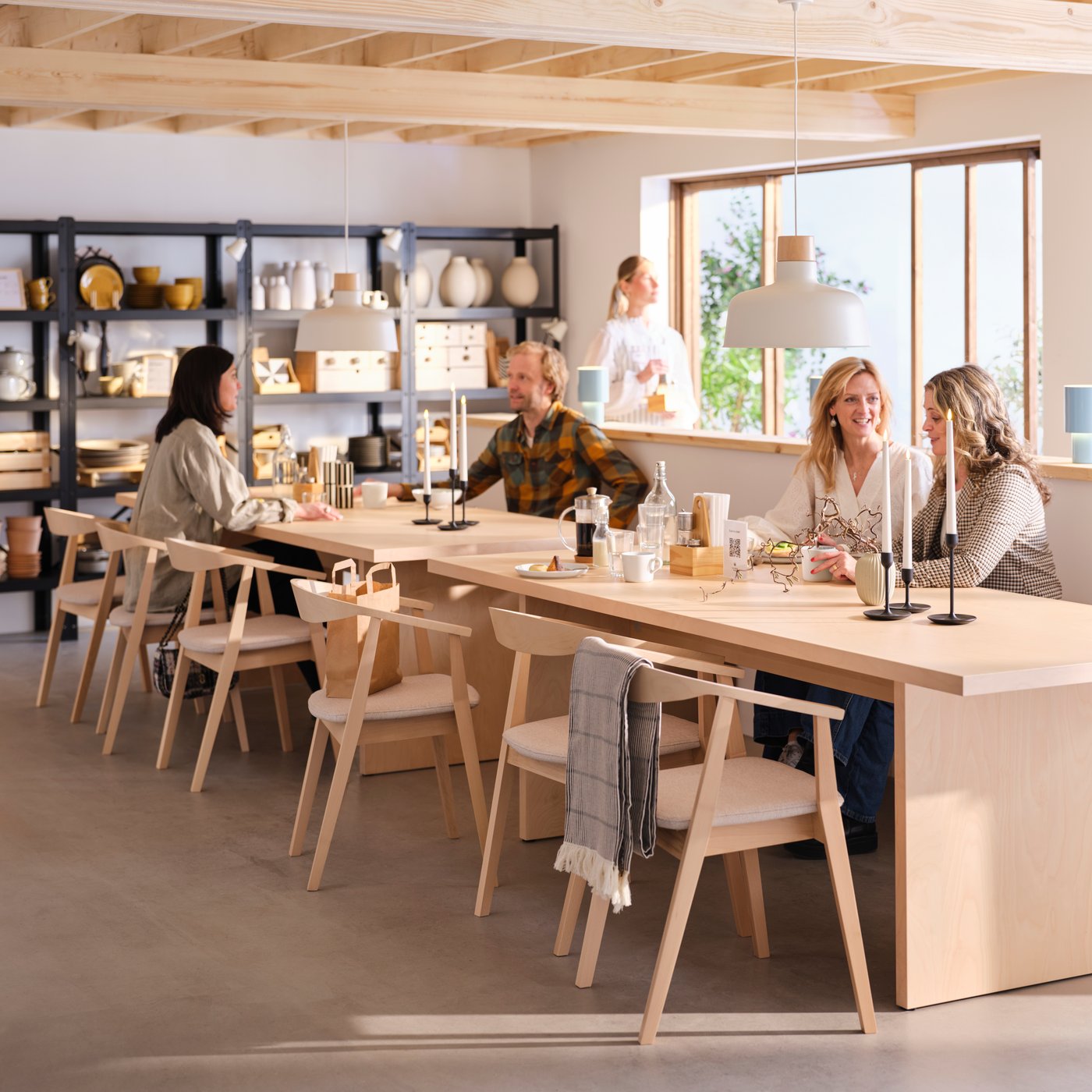 Several people sitting on STOCKHOLM chairs at BERGSHYTTAN tables in the light and spacious café section of a pottery shop.