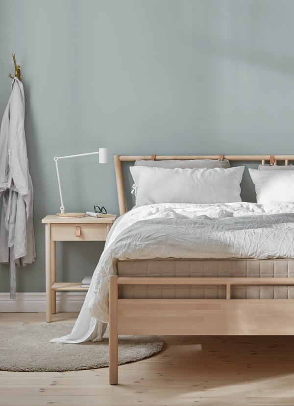 In einem Raum steht ein Bett aus Holz. Daneben steht ein BJÖRKSNÄS Nachttisch und eine Tischlampe darauf.