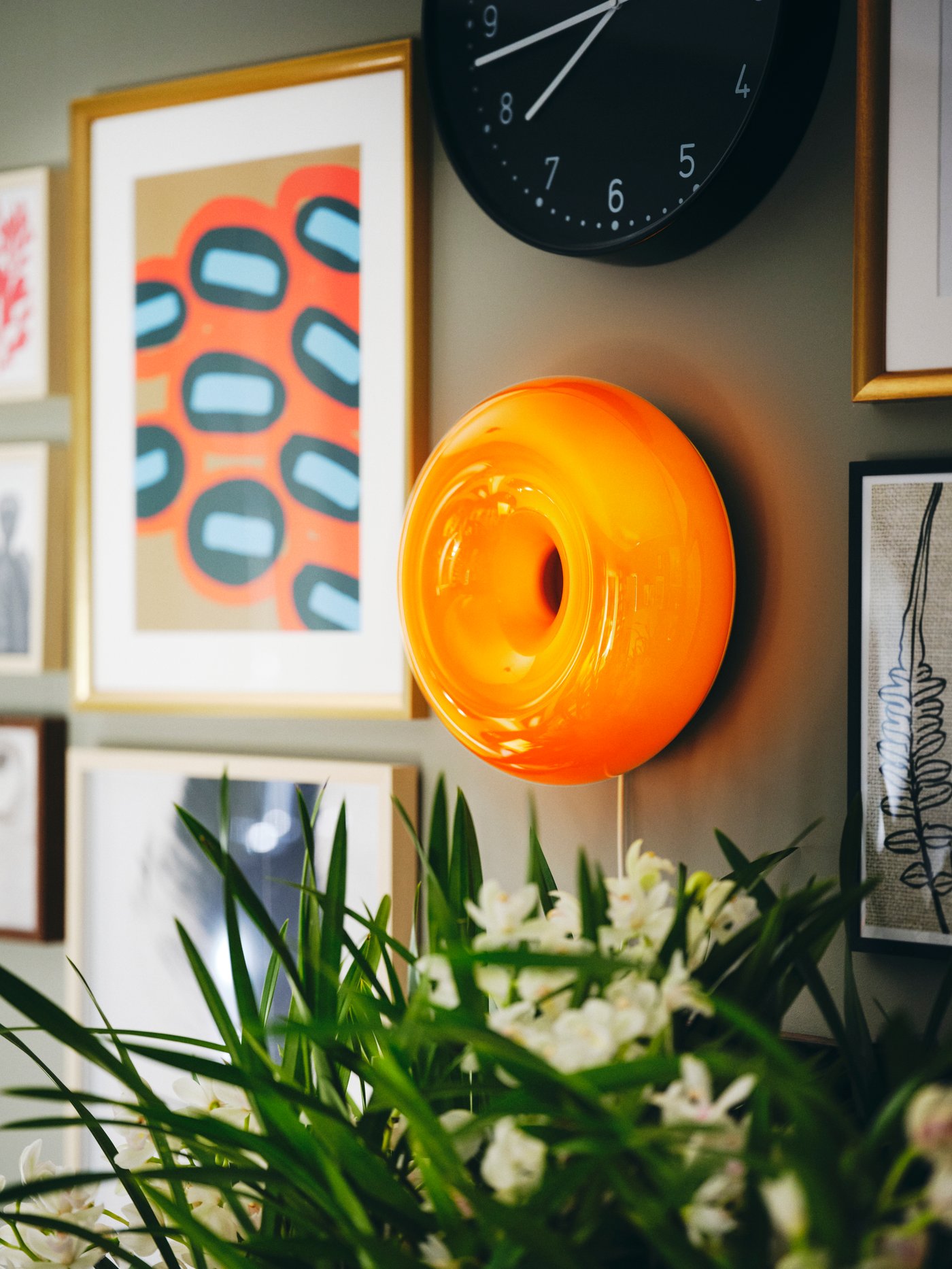 Runde orange VARMBLIXT Leuchte und gerahmte Poster an der Wand.