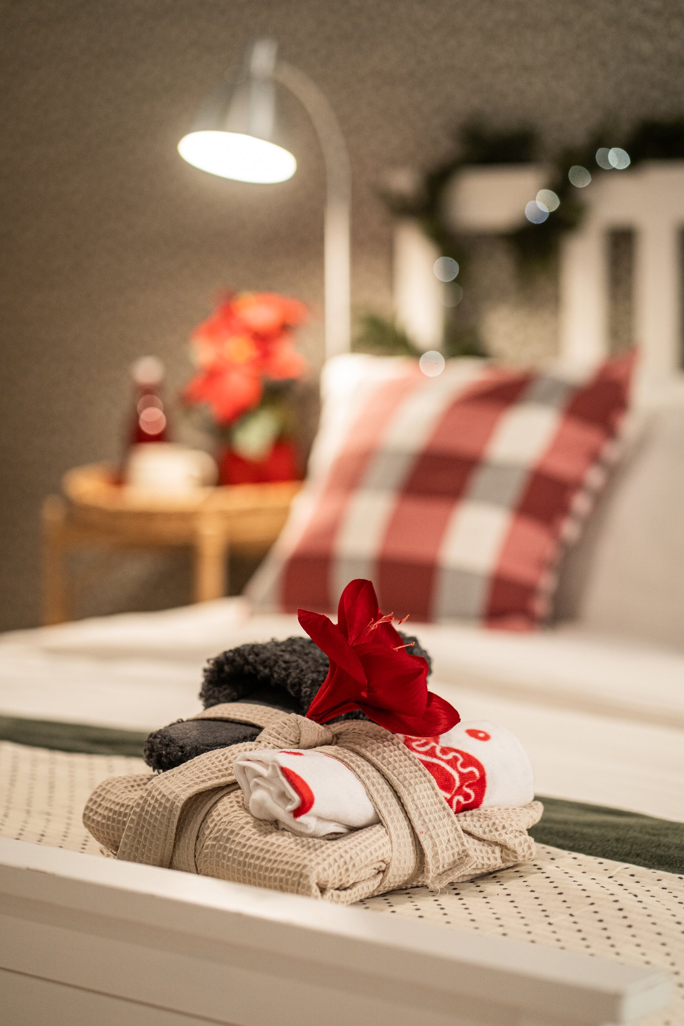 A mixed patterns white/red VINTERFINT hand towel on a bed with white sheets and a floor lamp in the background.