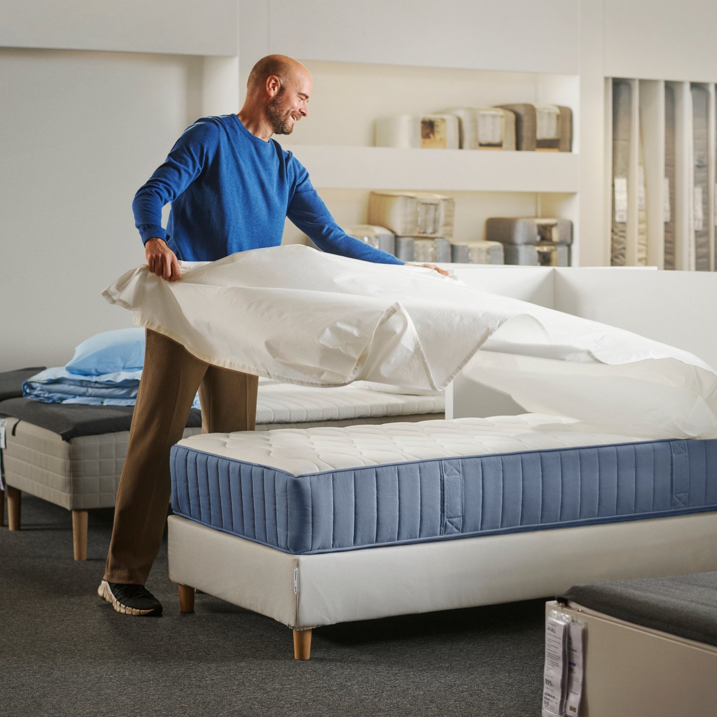 A person covering a VÅGSTRANDA pocket sprung mattress with a bedsheet in a store setting.