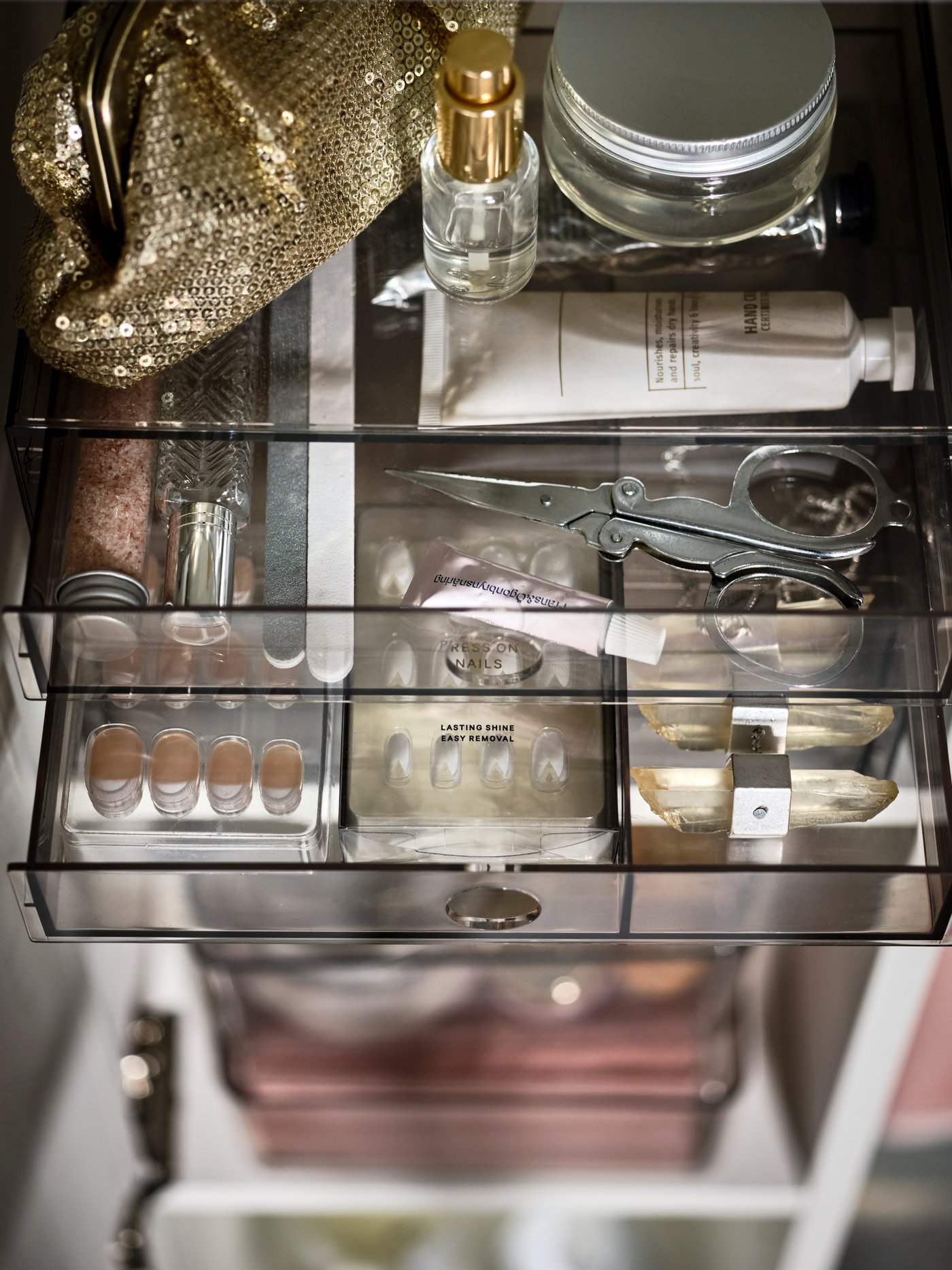 Es ist ein GODMORGON Kasten mit Fächern zu sehen, auf dem ein goldbrauner Geldbeutel liegt. Im Inneren befinden sich eine Schere und verschiedene Make-up- und Körperpflegeprodukte.