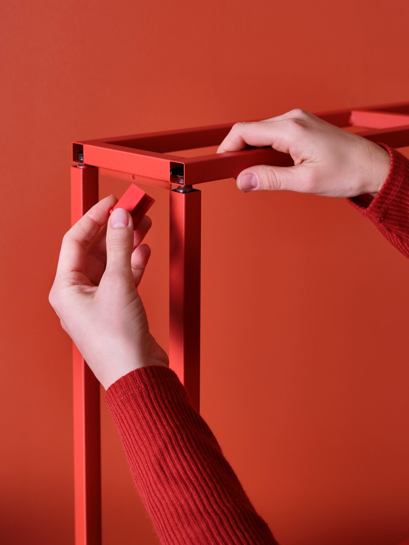 A person in red sweater assebly a red furniture in front of a red wall. 