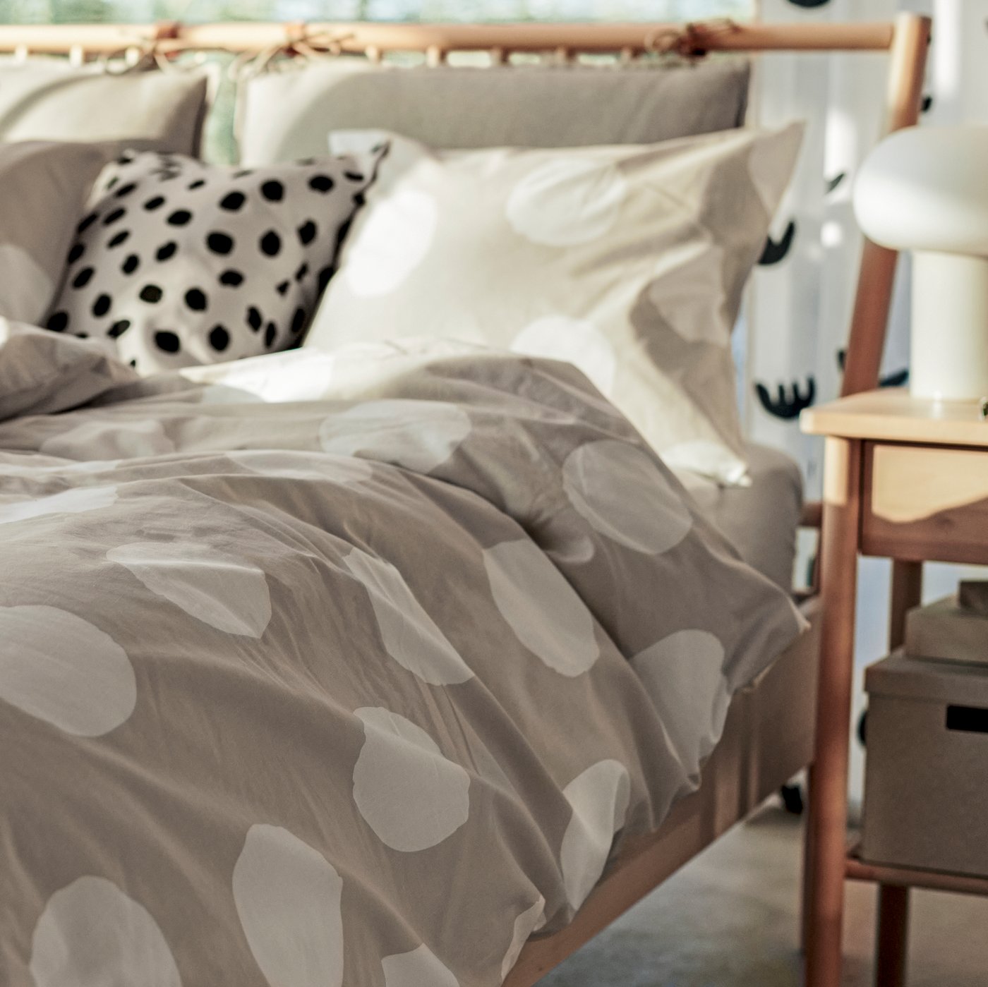 Una estructura de cama BJÖRKSNÄS de abedul/Luröy vestida con ropa de cama KLYNNETÅG beige/blanca/de lunares junto a una mesita de noche BJÖRKSNÄS.