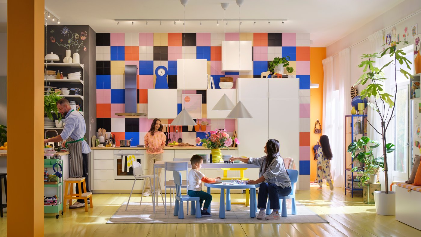 A family of five spends time together in a white modern kitchen with large, brightly coloured tiles and a high ceiling.