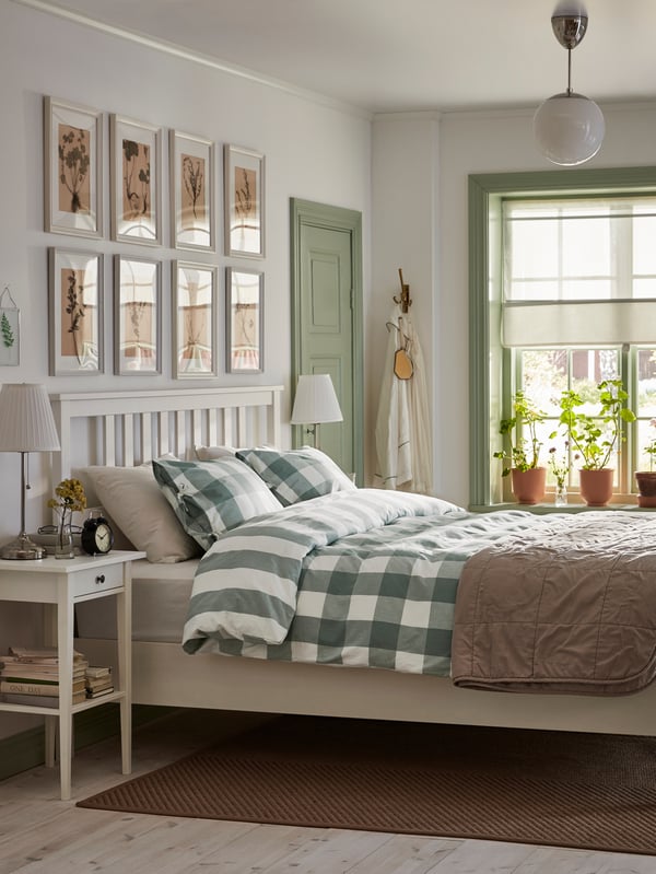 A white HEMNES bed sits in an airy white bedroom. A white and green checkered bedspread is neatly made on the bed.