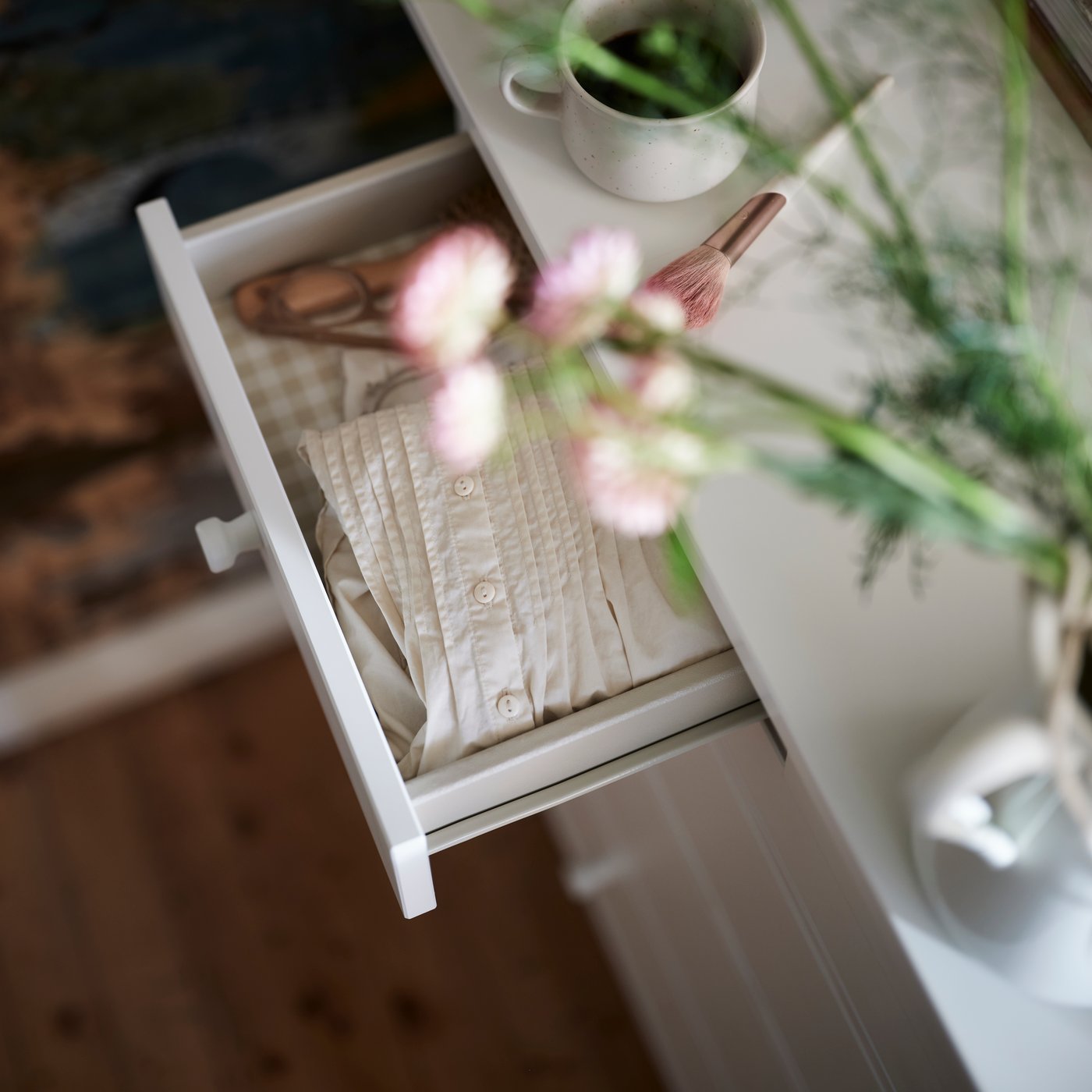 A GULLABERG chest of 6 drawers in white with one drawer pulled out, shown with a plant above in a rustic room setting.