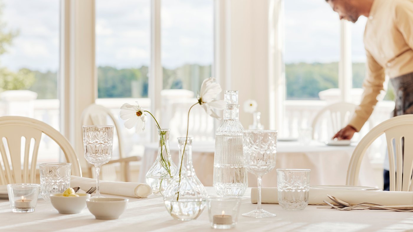 En mand er ved at dække nogle borde i charmende lys og nostalgisk badehotelstil.