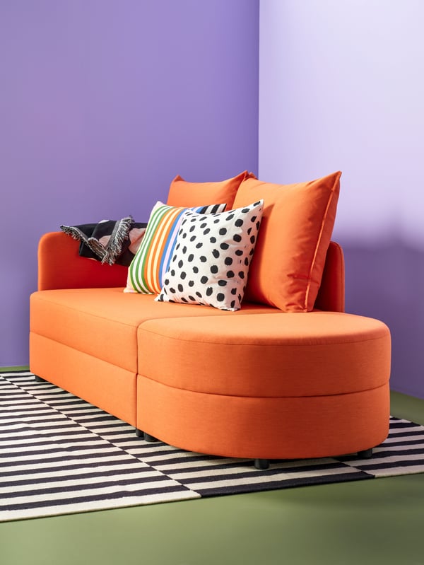 A sofa in trendy orange against a purple wall.