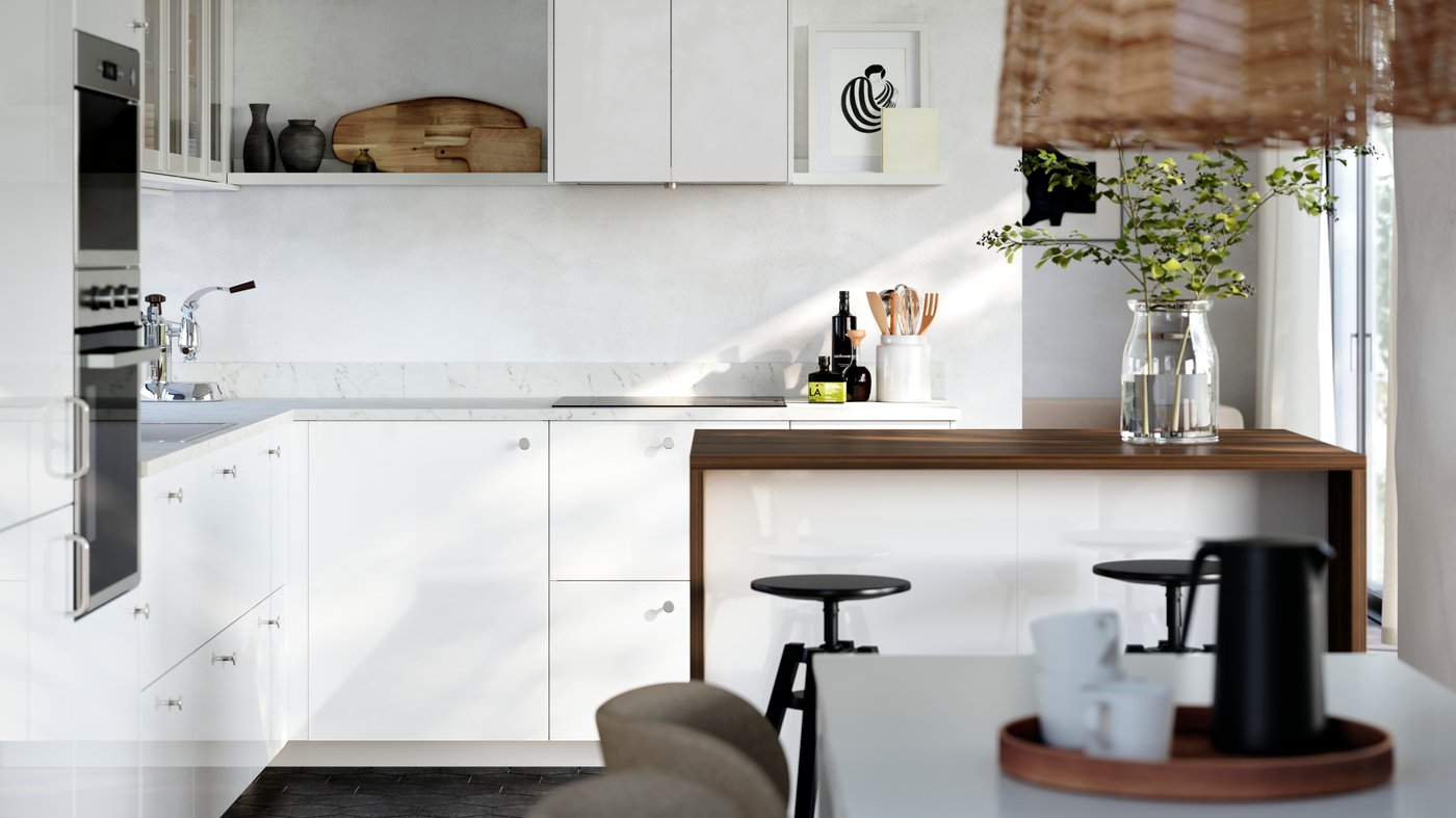 A kitchen with white high-gloss RINGHULT fronts and HEJSTA glass doors has a picture ledge on the wall and a kitchen island.