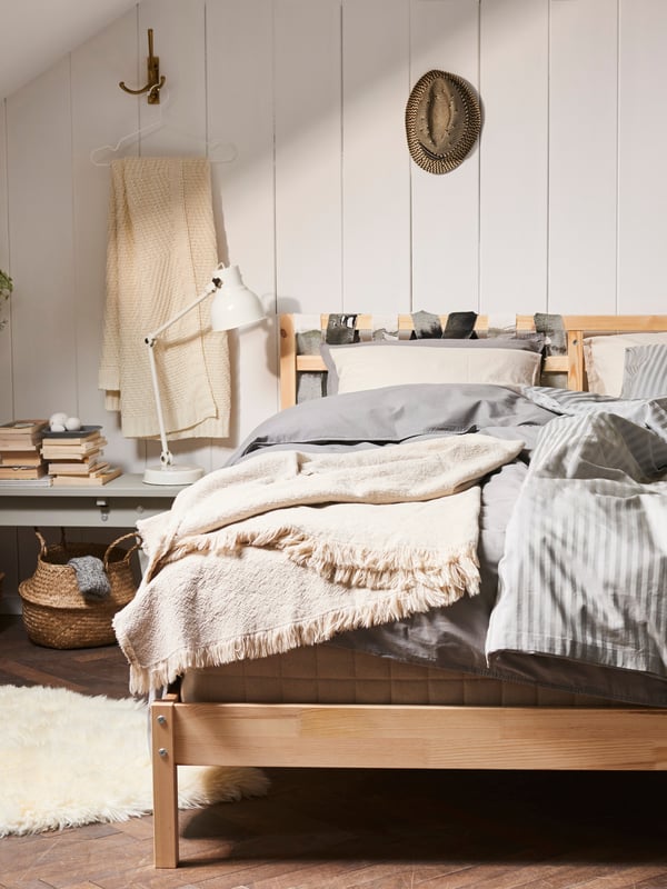 Ein Schlafzimmer im skandinavischen Stil mit einem Holzbett und vielen Decken und Plaids aus natürlichen Materialien für Boho Akzente..