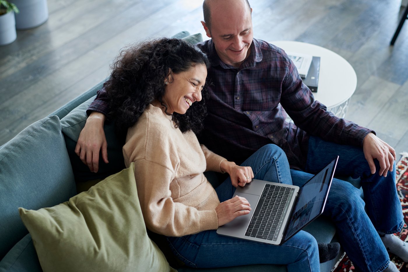 A couple sitting on a blue sofa while looking at a laptop