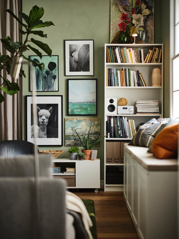 Woonruimte met witte BILLY boekenkast met daarin boeken en een speaker, tegen een wand met ingelijste prints en foto’s.