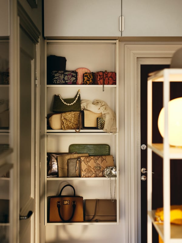 A handbag collection on two white ENHET wall frames with shelves below ENHET wall cabinets with white ENHET doors.