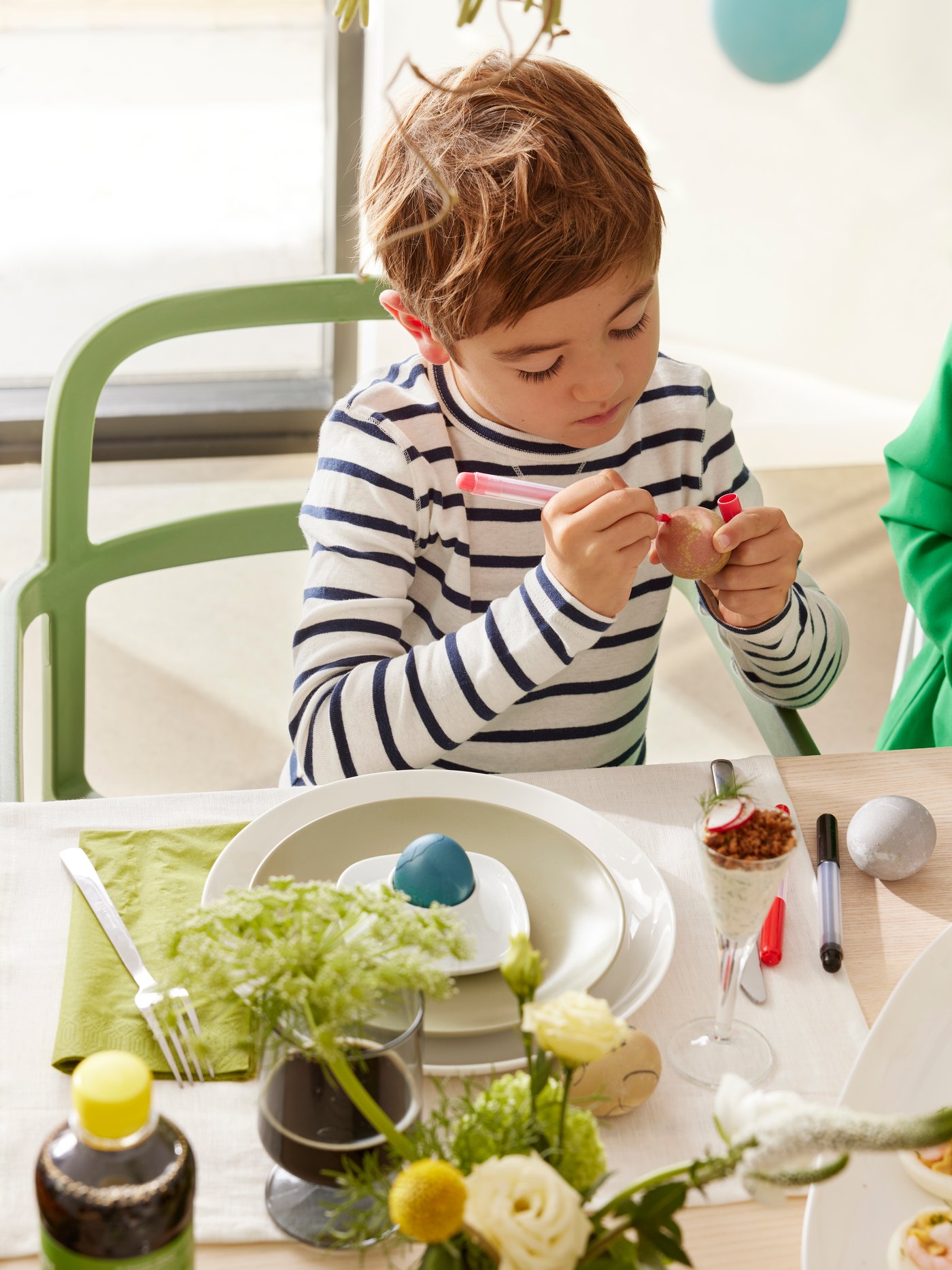 A young boy is painting Easter eggs with mixed colours, MÅLA felt-tip pen.