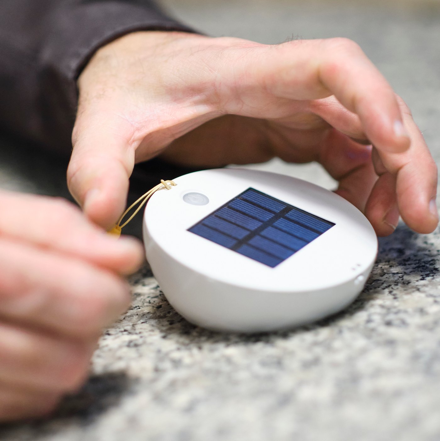 Tangan seseorang meletakkan pencahayaan berkuasa solar LED SAMMANLÄNKAD di atas meja rupa granit dengan panel solar menghadap ke atas.