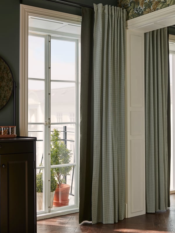 A green BLÅHUVA block-out curtain and a patterned ORDENSFLY curtain hang by a balcony door for customised light and privacy.