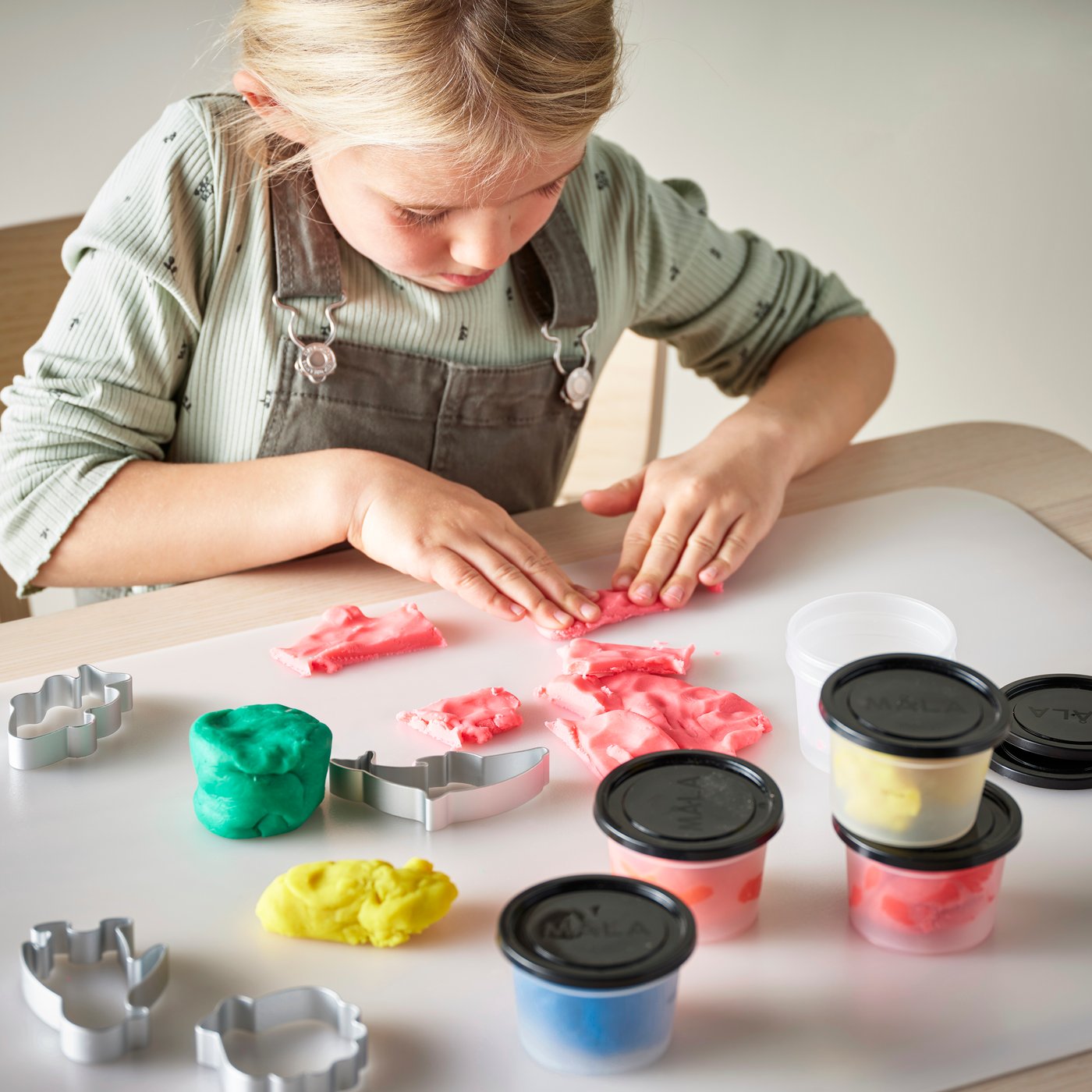 Una niña está sentada en una mesa modelando figuras con masa para moldear MÅLA de colores.
