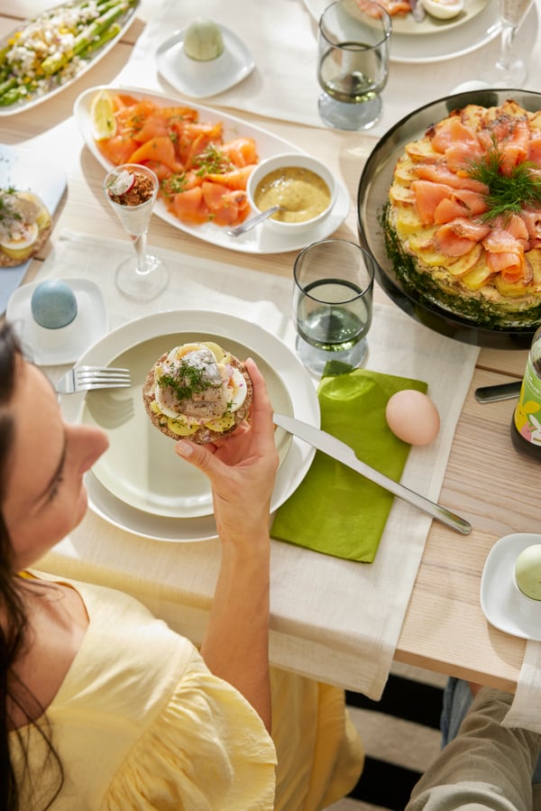 Woman's hand holding a crispy bread sandwich, with other Easter foods served on the table.