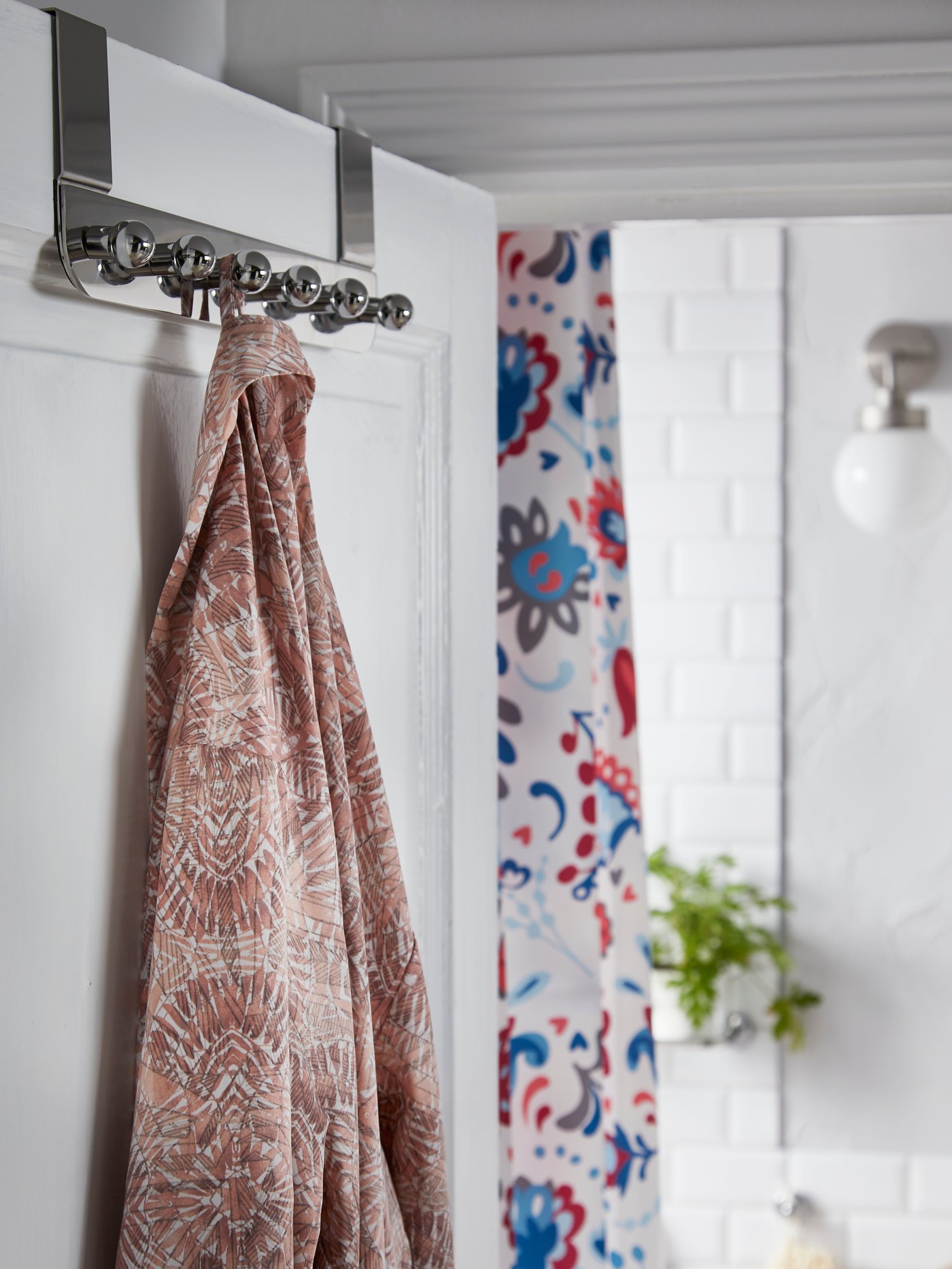 VOXNAN hanger for the door in chrome effect hangs on the bathroom door and a patterned bath robe is hanging from it.