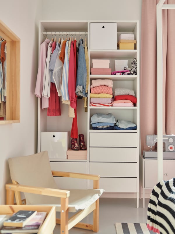 A white AURDAL wardrobe in a bright bedroom with clothes on the hanging rail and boxes and colourful clothing on shelves.