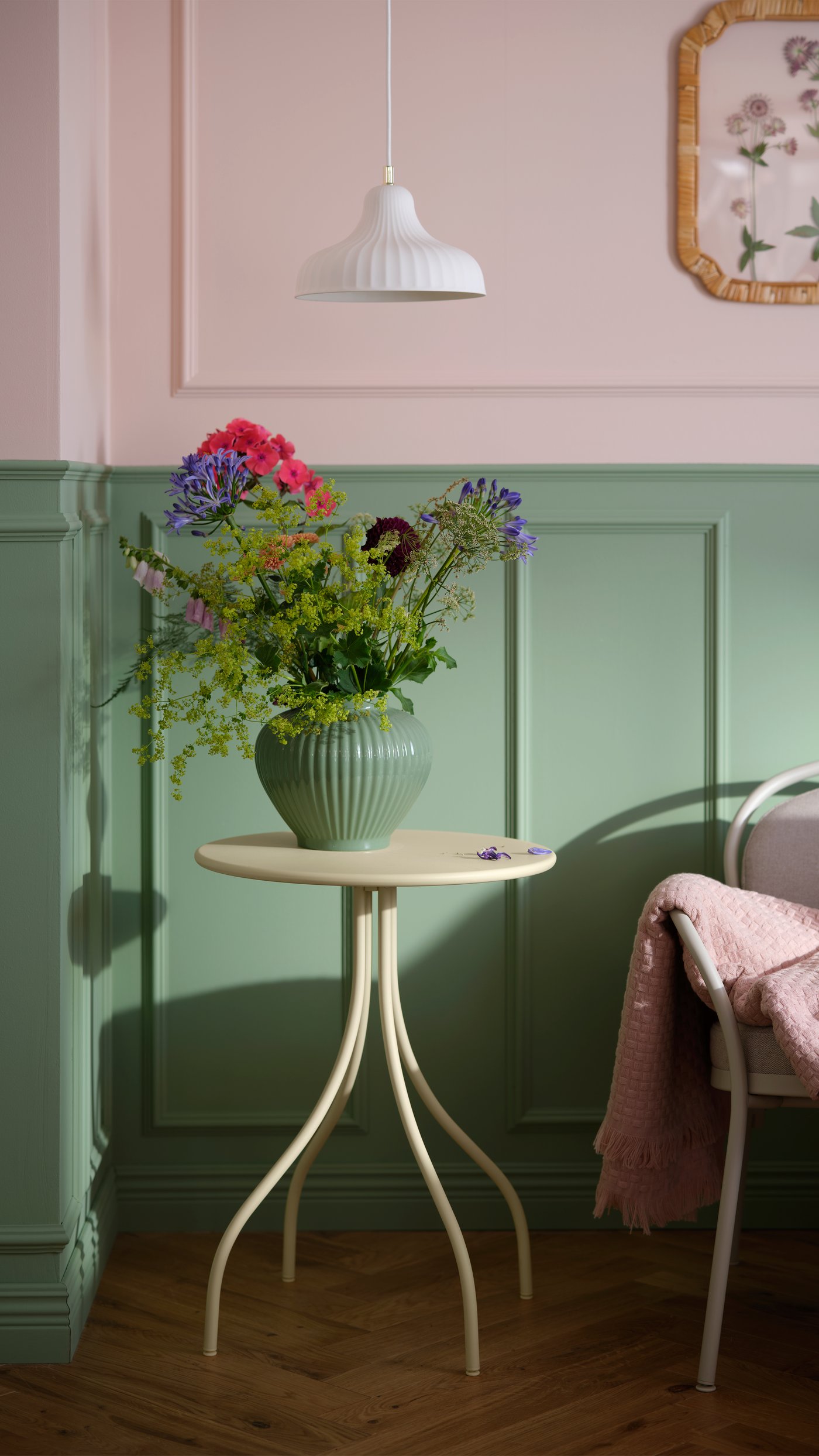 Ein Beistelltisch auf dem sich eine Vase in pastellgrün mit Blumen befindet.