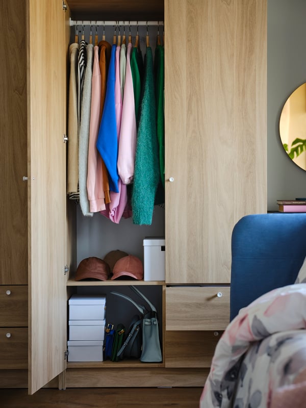Vêtements et trois boîtes à compartiments SPINNROCK blanches dans une armoire-penderie VILHATTEN effet chêne avec deux portes et deux tiroirs.