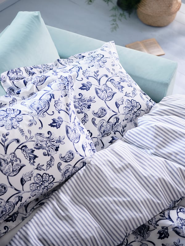 Angolo di un divano-letto con copripiumino e federe JUNIMAGNOLIA a motivo floreale bianco/blu scuro - IKEA