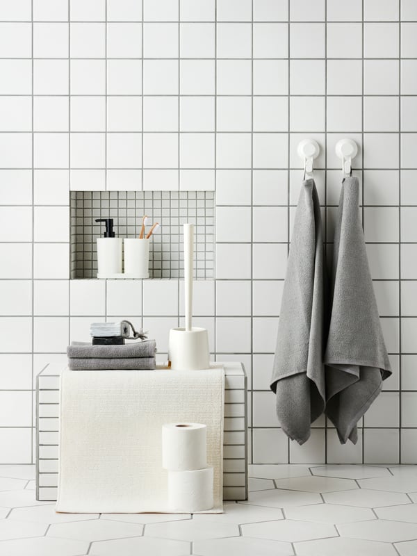 Geflieste Badezimmerwand mit einer Reihe TISKEN Haken mit Saugnapf, an denen Handtücher und Badutensilien befestigt sind.