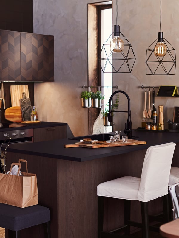 Une cuisine avec un tabouret de bar BERGMUND, un îlot pour cuisine avec plusieurs articles et des suspensions BRUNSTA noir avec ampoules.