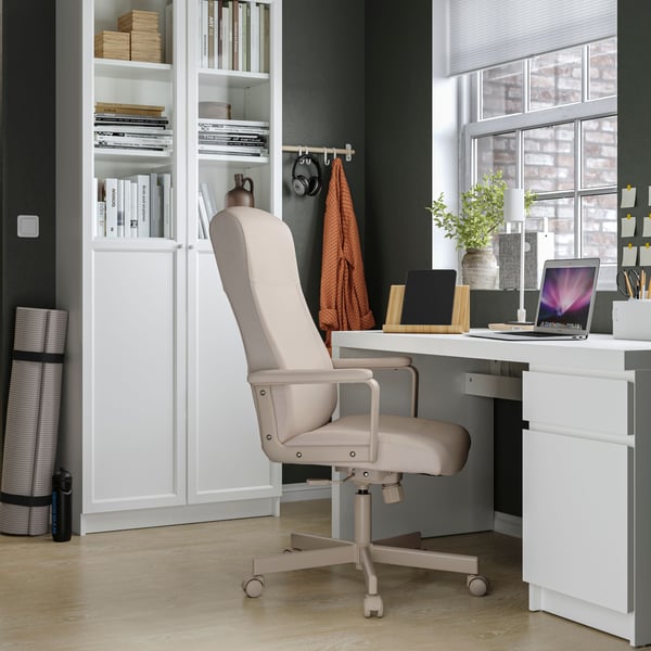 Una silla de escritorio MILLBERGET beige frente a un escritorio blanco.